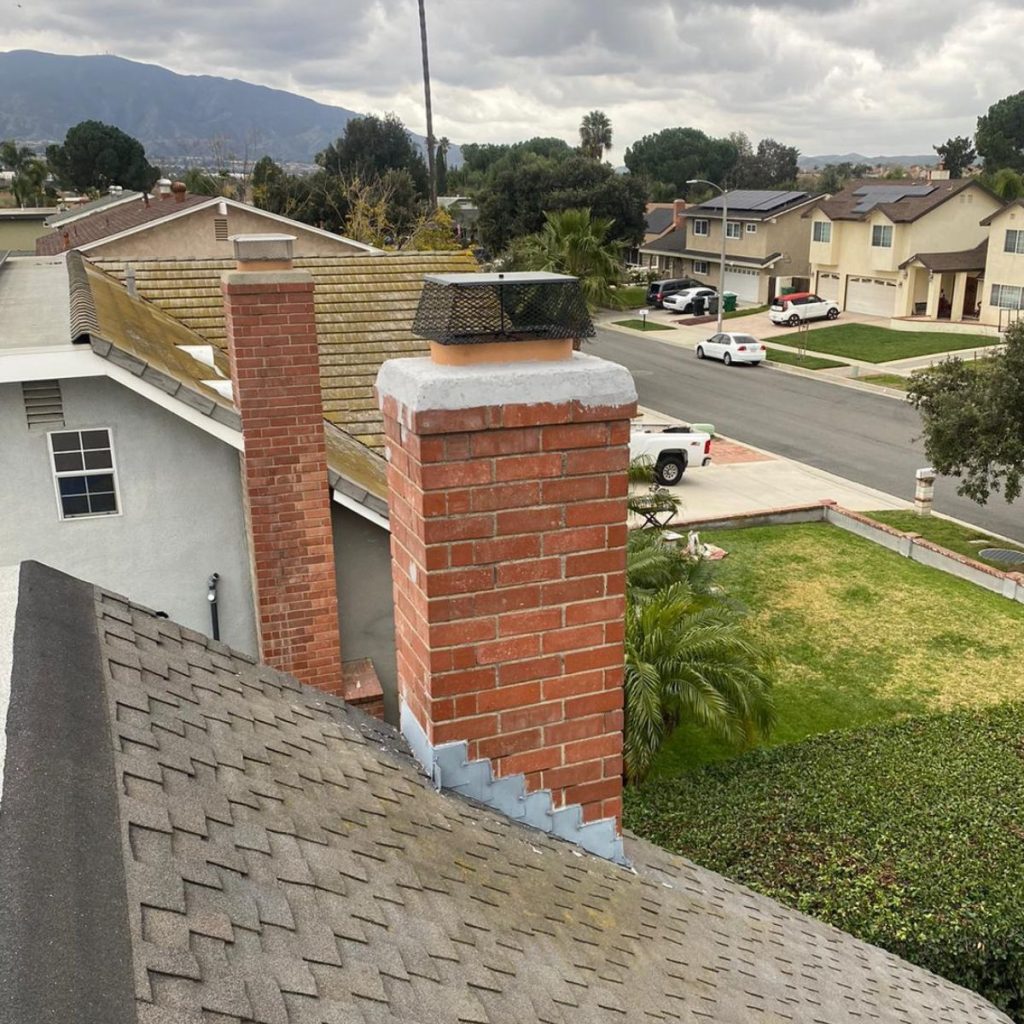 Red brick chimney with new crown and black chimney cap on residential roof.