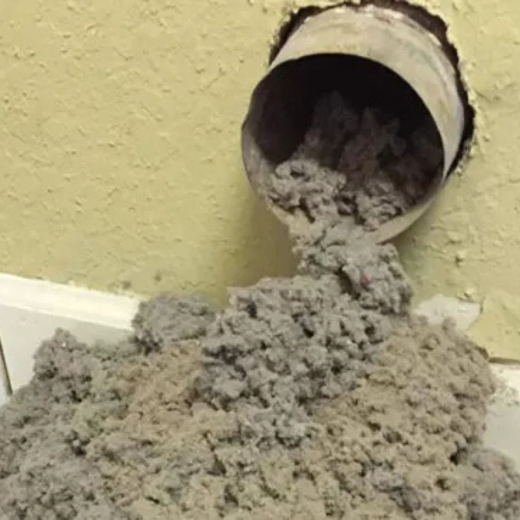 Dryer vent pipe overflowing with lint buildup against wall