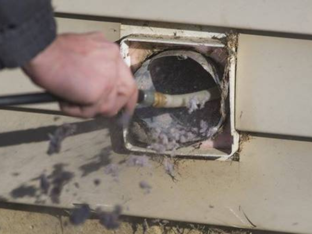 Hand cleaning lint from exterior dryer vent opening.