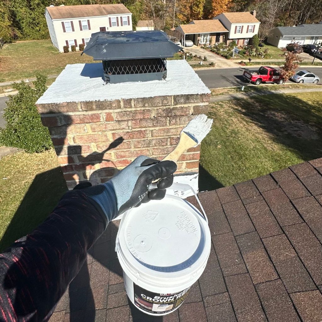 Hand applying chimney crown sealer on brick chimney for waterproof protection.
