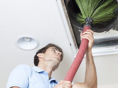 Technician using rotary brush to clean ceiling air duct