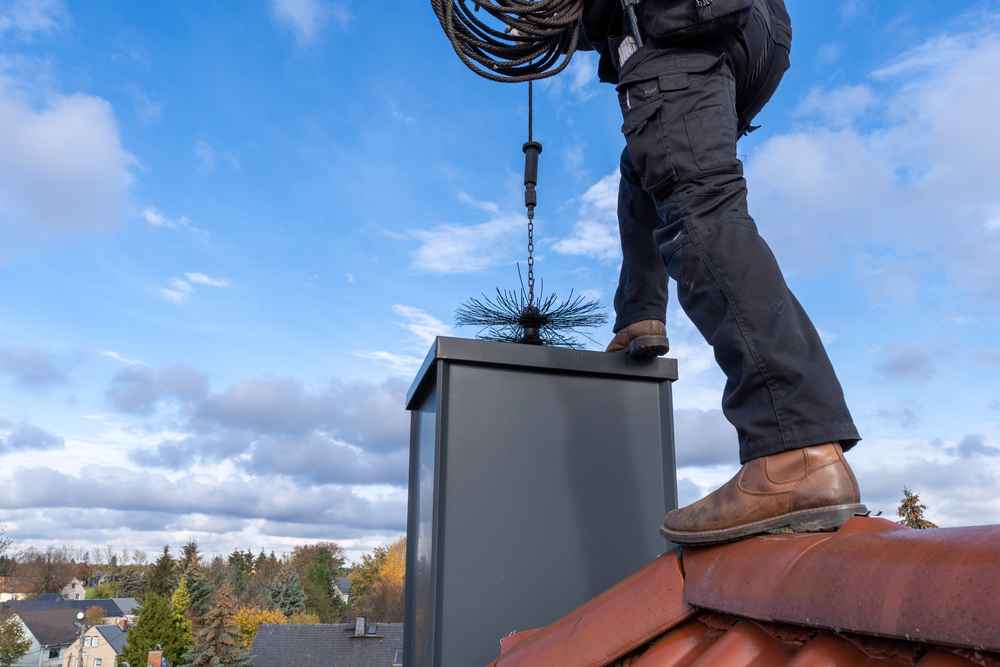 Chimney sweep cleaning a rooftop chimney with professional brush.