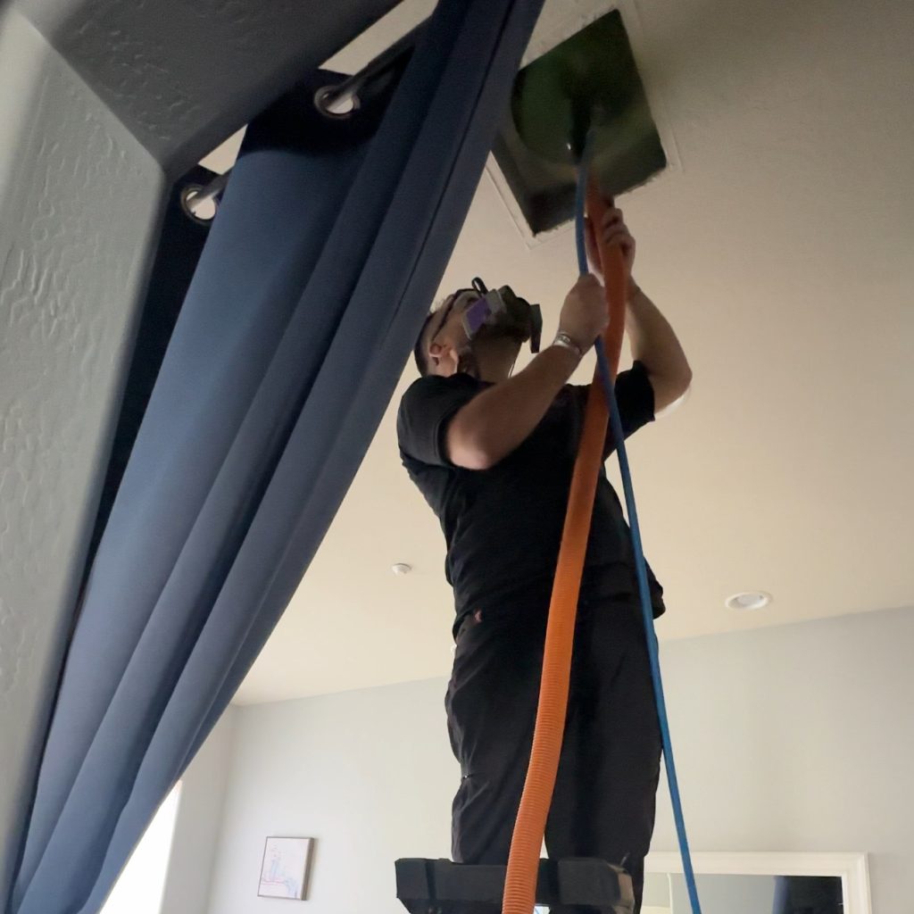 EcoAirClean technician cleaning ceiling air duct with vacuum hose