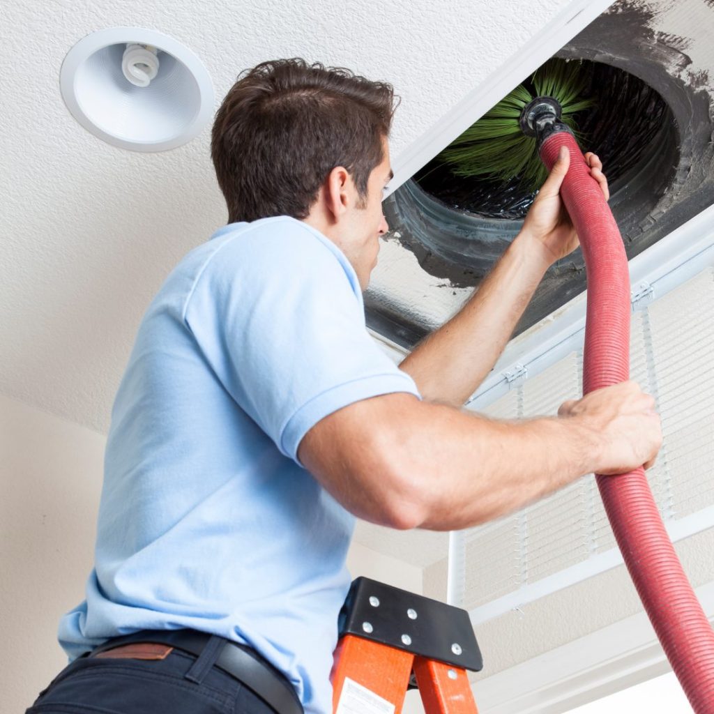 Technician using vacuum hose and brush to clean ceiling duct